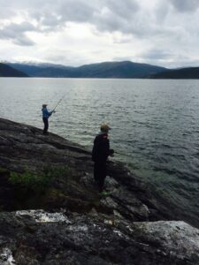 To personer står og fisker på svabergene