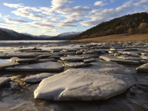 Isgang på Sund, isblokker ligger igjen på stranda etter at vatnet har trukket seg tilbake. Blå himmel med noen skyer, åser og fjell i det fjerne.