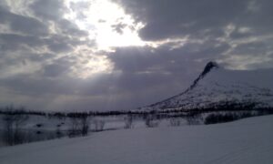 Fjellet Kongsen og sola som bryter gjennom skyene